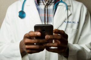 personne portant une blouse de toilette avec un stéthoscope vert sur le cou utilisant un téléphone en position debout