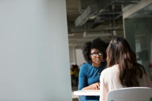 Deux femmes engagées dans une discussion dans un environnement de bureau moderne, mettant l'accent sur la communication et l'interaction.