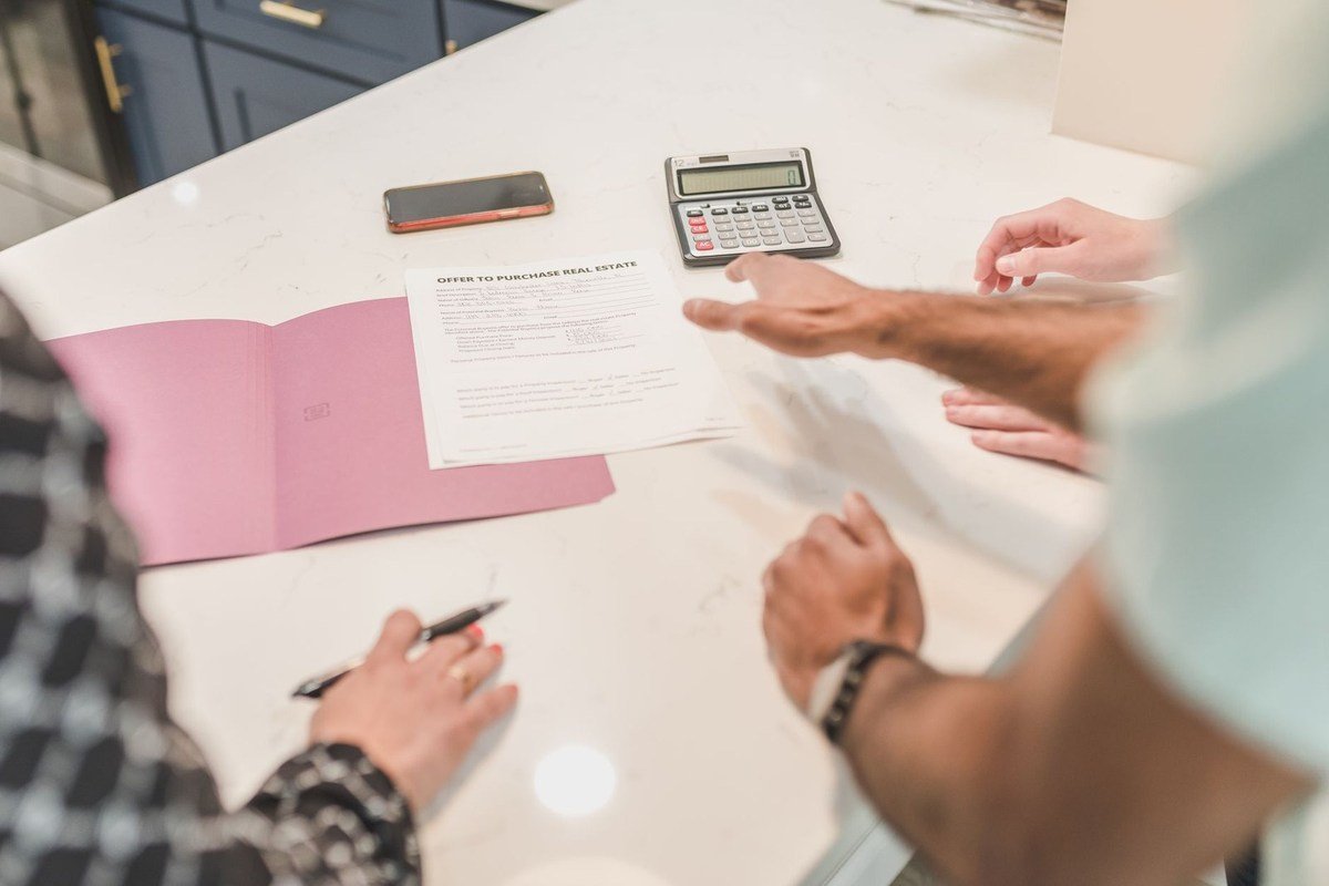 Deux personnes discutent autour d'un document, d'un livre et d'une calculatrice sur une table blanche