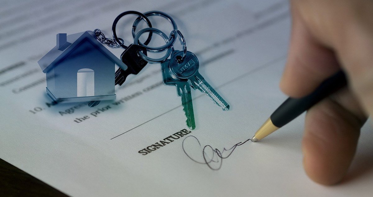 Clés de maison sur un document signé, main tenant un stylo au-dessus