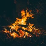 Feu de camp nocturne avec flammes orangées, bois et braises rougeoyantes
