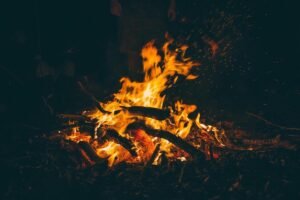 Feu de camp nocturne avec flammes orangées, bois et braises rougeoyantes