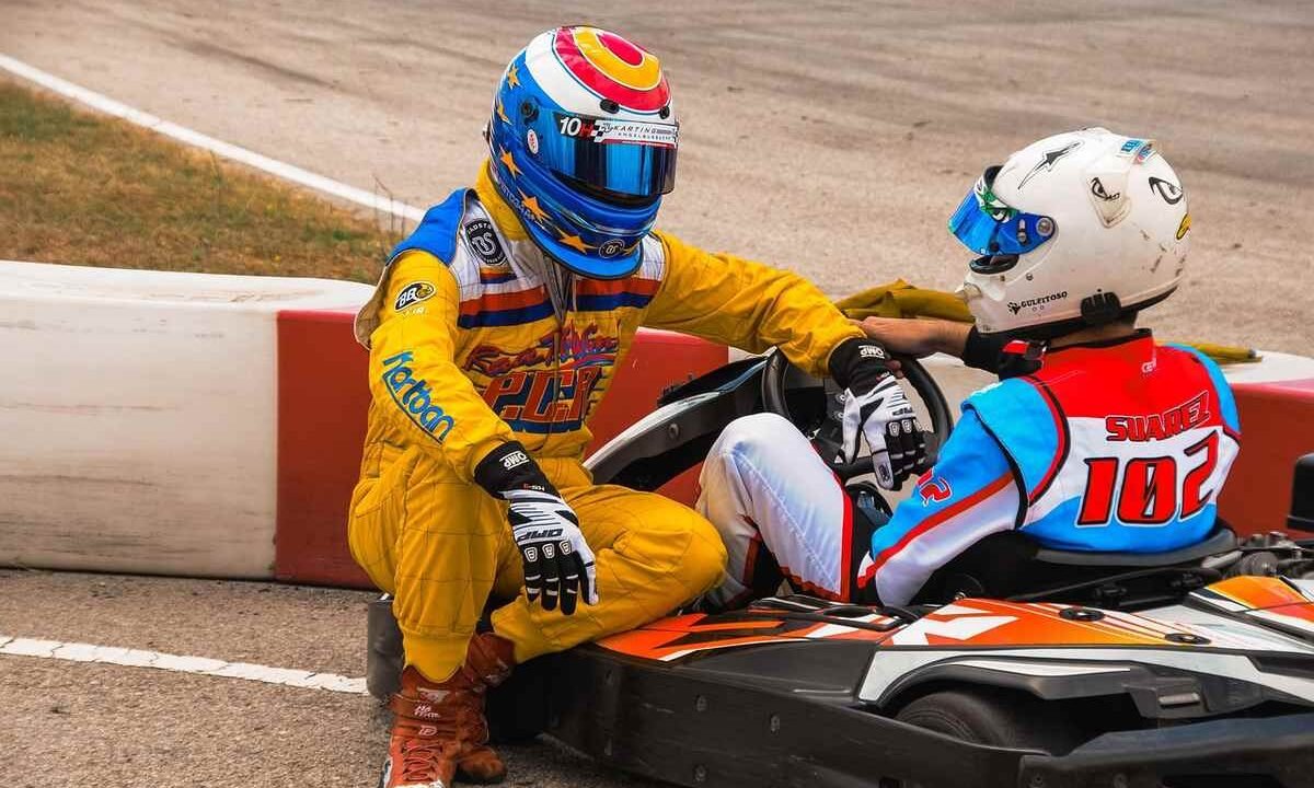Un pilote en jaune aide un concurrent assis dans un kart rouge