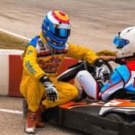 Un pilote en jaune aide un concurrent assis dans un kart rouge