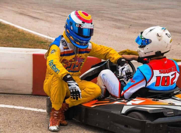 Un pilote en jaune aide un concurrent assis dans un kart rouge