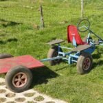Un kart bleu tracte une remorque rouge sur gazon avec siège rouge