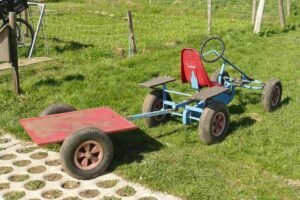 Un kart bleu tracte une remorque rouge sur gazon avec siège rouge