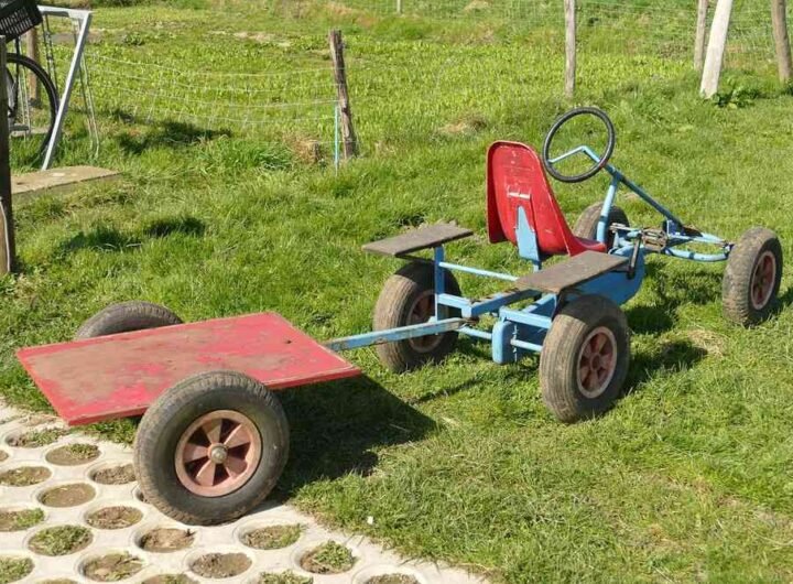 Un kart bleu tracte une remorque rouge sur gazon avec siège rouge